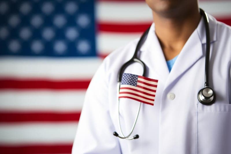 Physician in a white coat in front of a U.S. flag